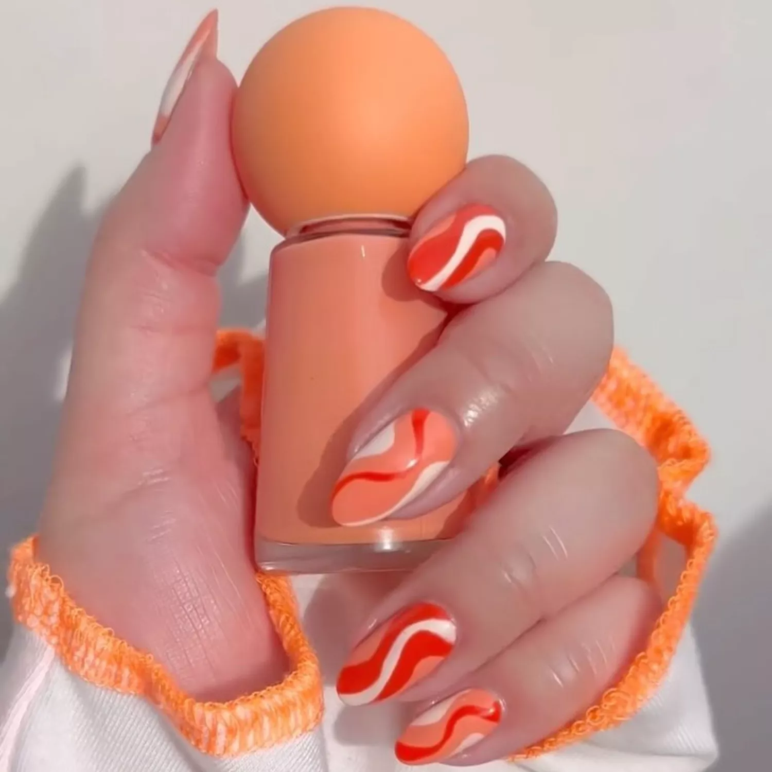 Peach swirl manicure holding a nail polish bottle