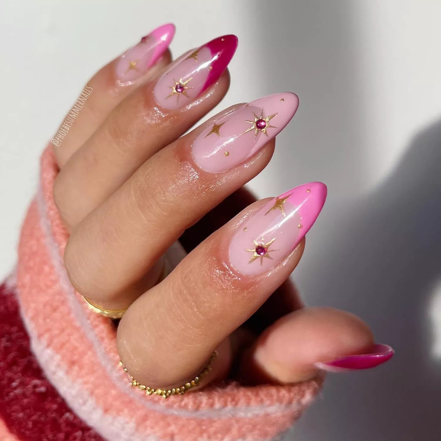 close up of nails with light pink base and various shades of pink as french tip, gold stars and pink rhinestones