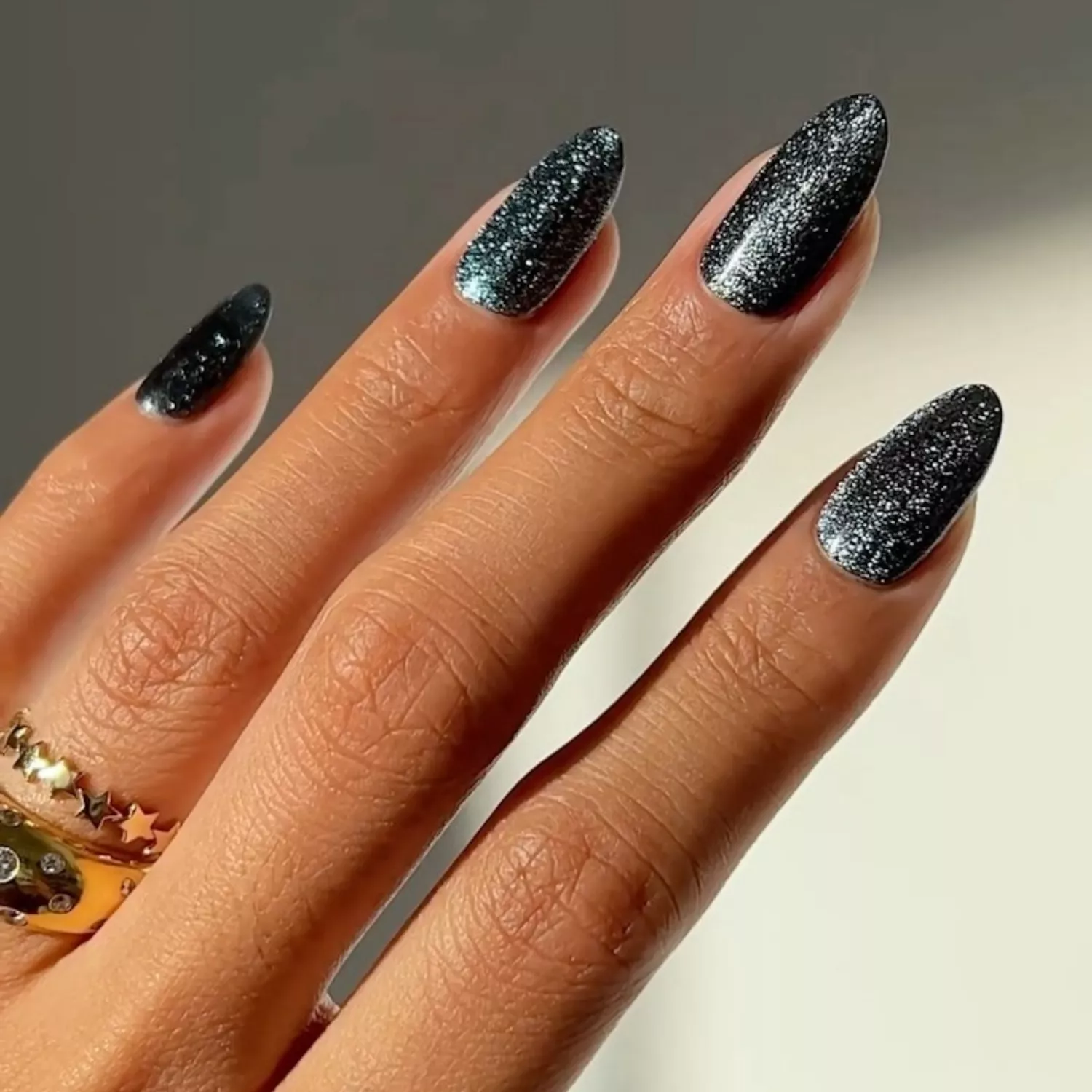 Black and silver glitter manicure with layered gold rings on finger