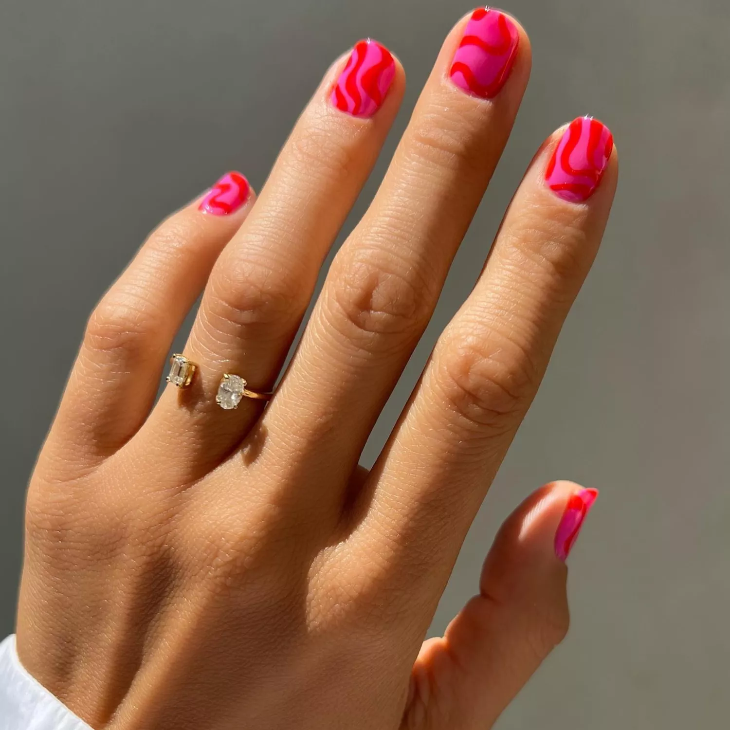 close up of nails with hot pink base and thick red swirls on top