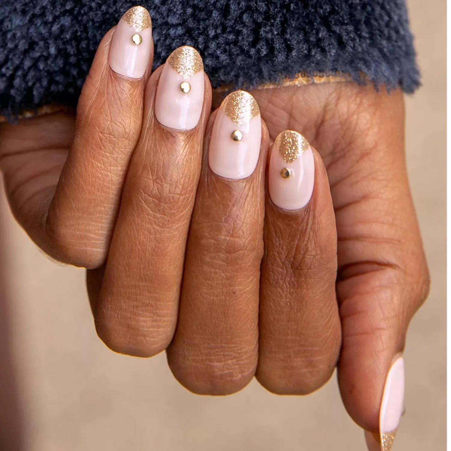 Manicure with neutral base, gold art deco fan design, and gold studs