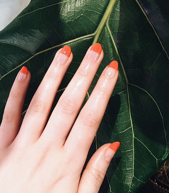 Hand with orange manicure against leaf