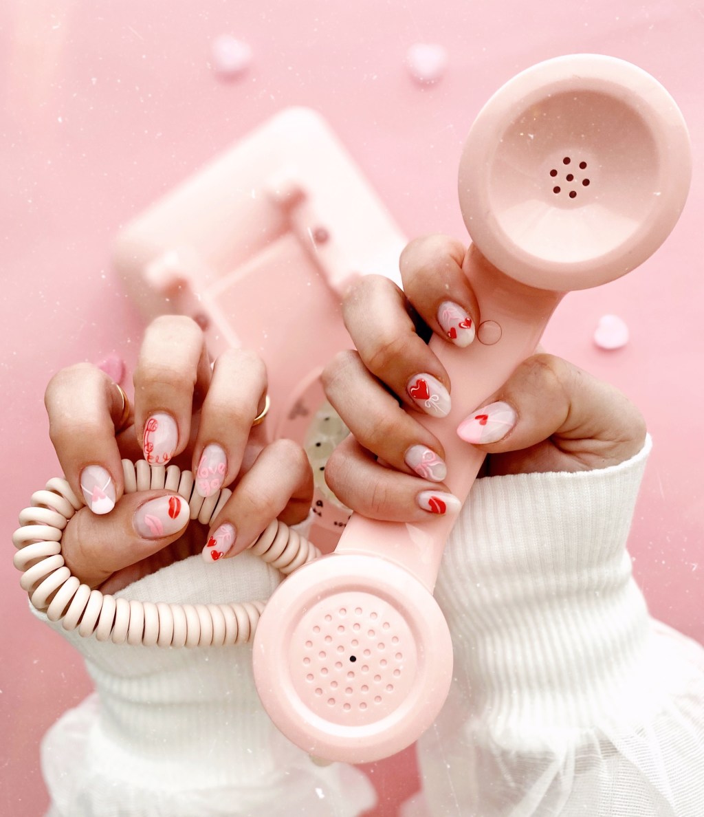 cute red and pink Valentines Day nails with mismatched Vday nail art including hearts, kisses, and bows