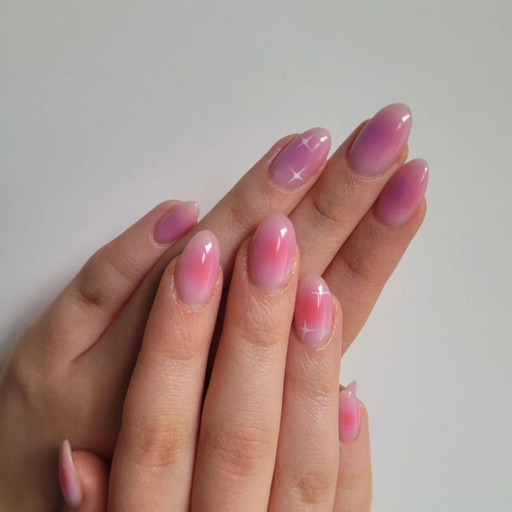 light pink almond shaped aura nails with a white celestial star design and subtle purple hue colors