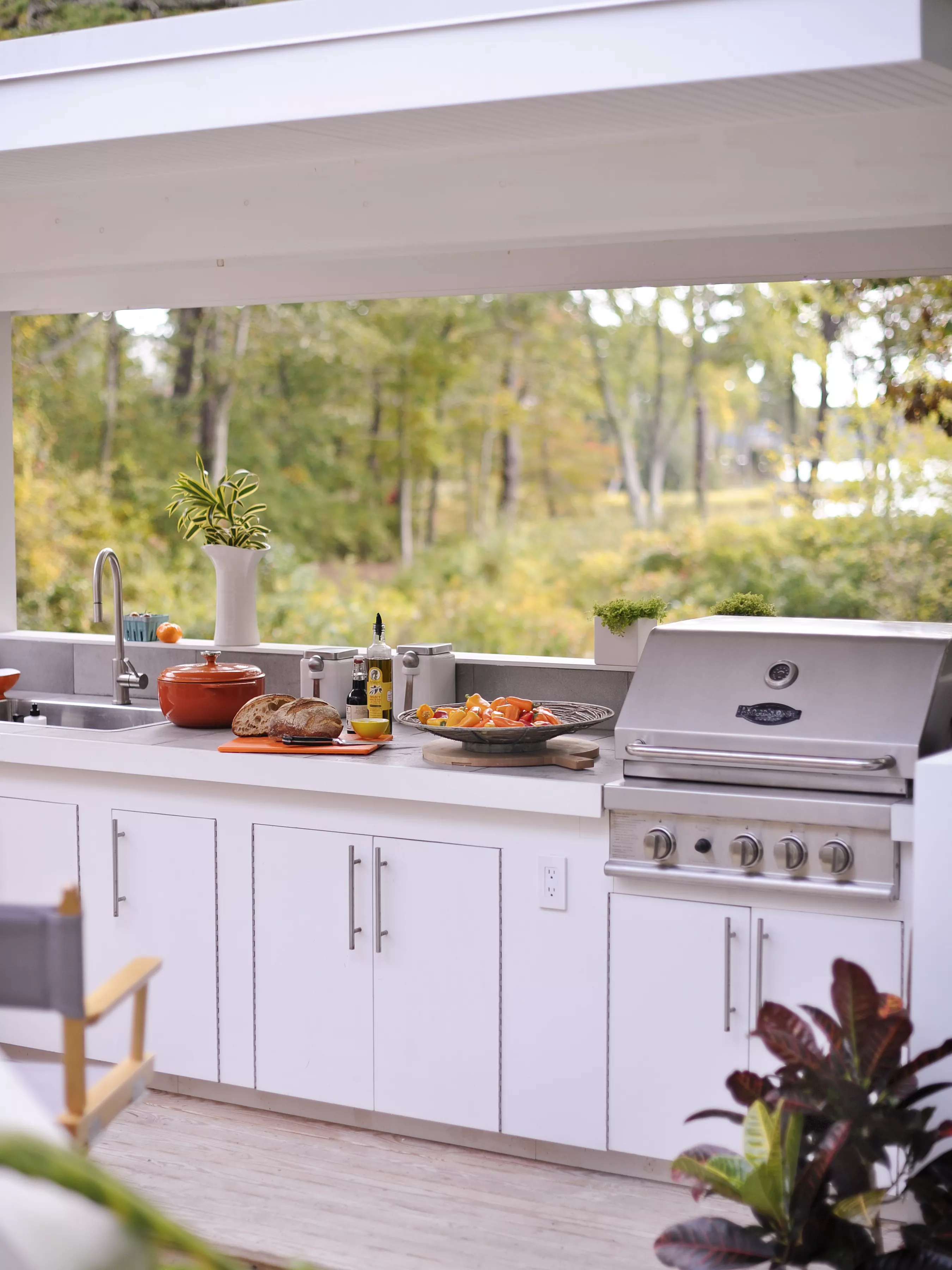 Outdoor kitchen overlooking trees and water with a stainless steel grill and food on the countertops.