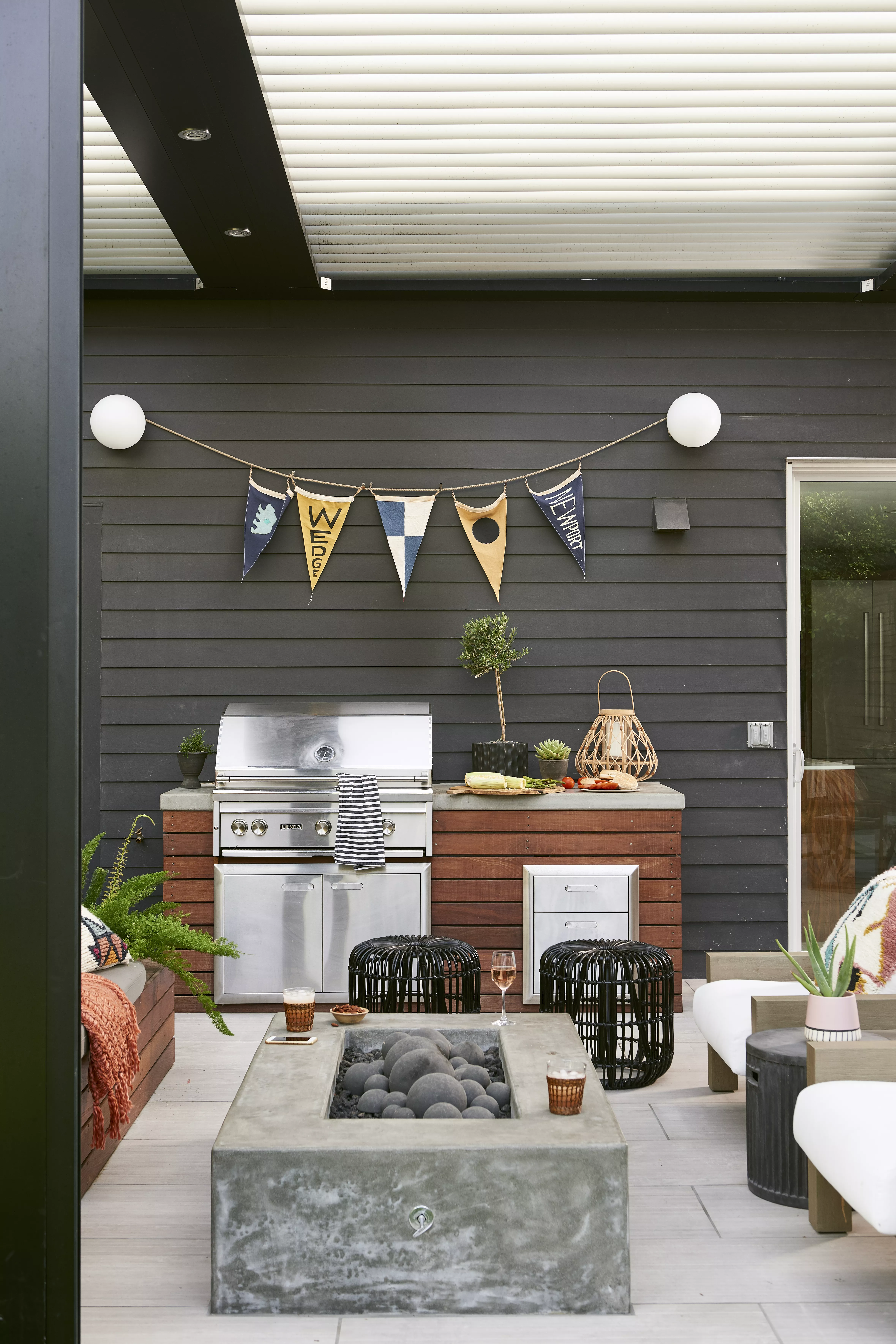 Covered patio with rectangular stone fire pit in foreground with built-in grill cooking area in background