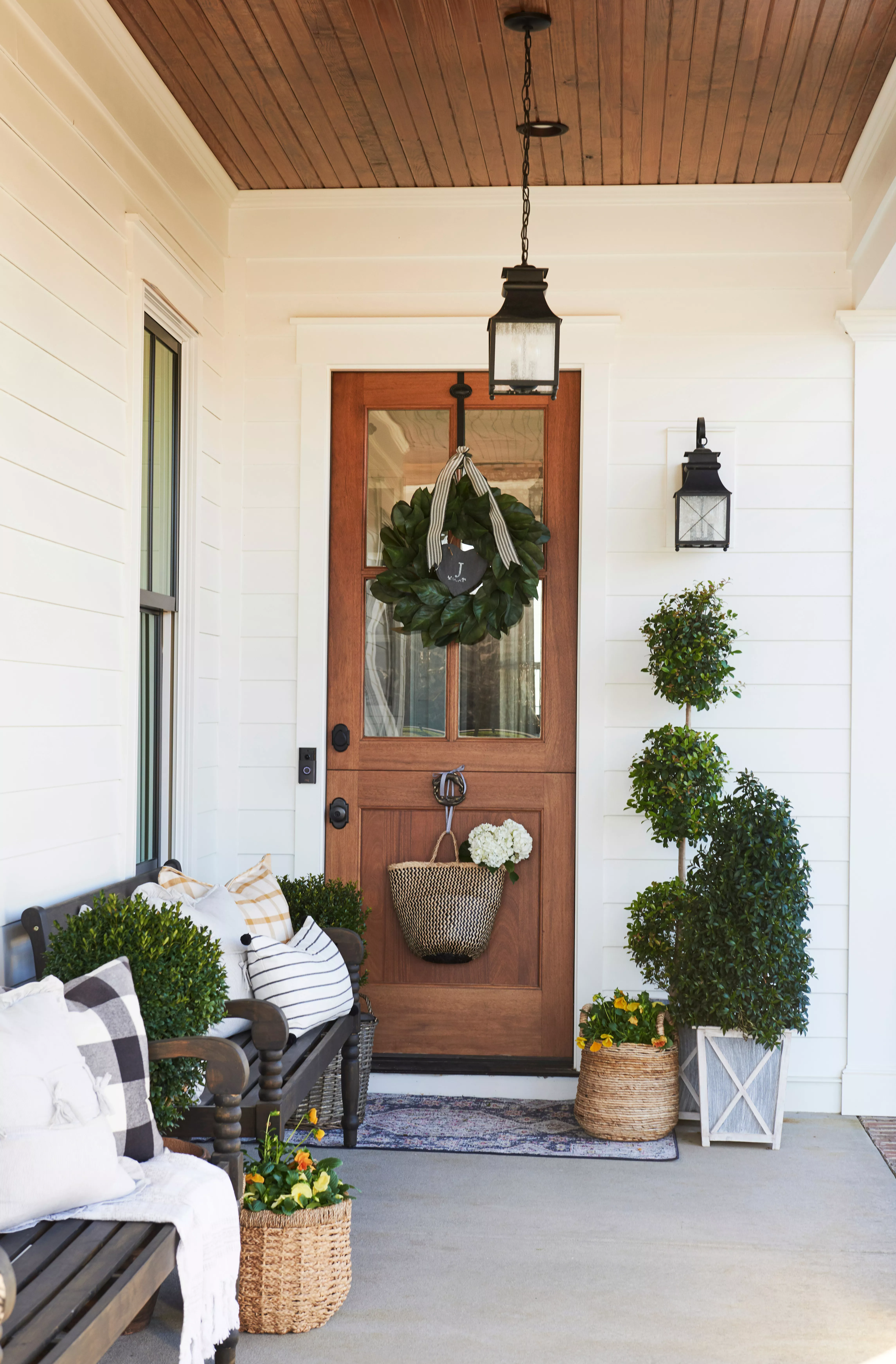 Front door with a bench, topiaries, and a wreath