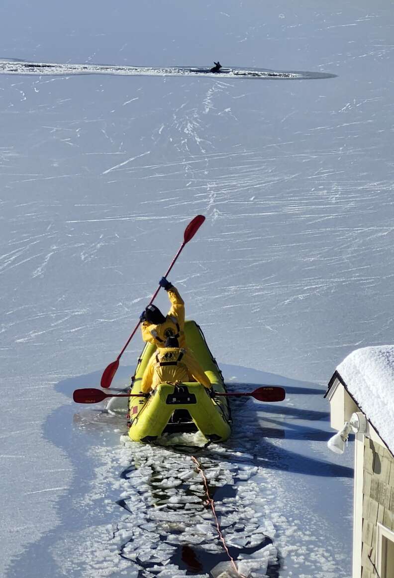 Firefighters in yellow boat breaking through ice toward deer in the distance