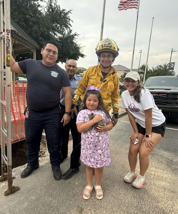 Family standing with firefighters with little girl in the middle holding gray kitten